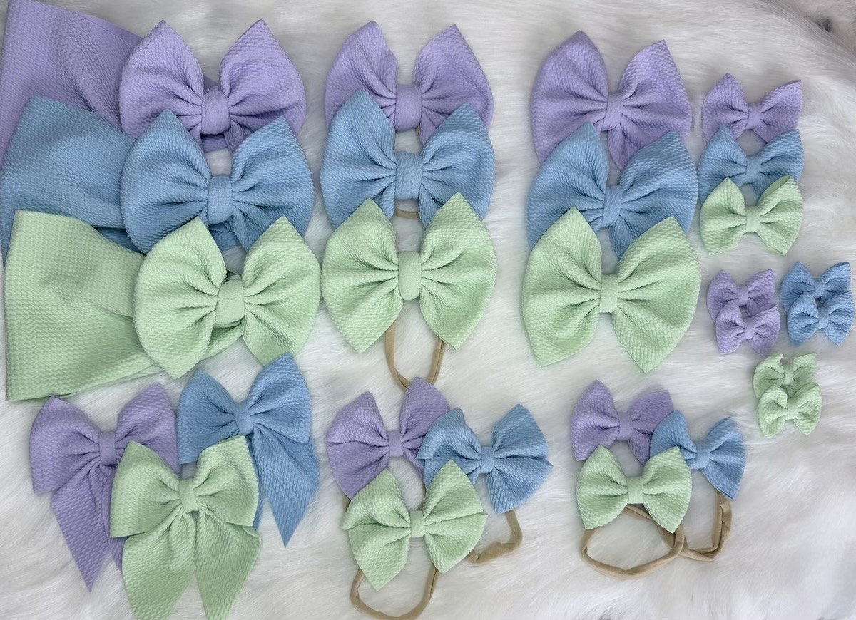 Handmade pastel baby hair bows in lavender, baby blue and mint green β large bows, mini bows and nylon-headband sets arranged on soft white faux fur by Little Addie's Bows